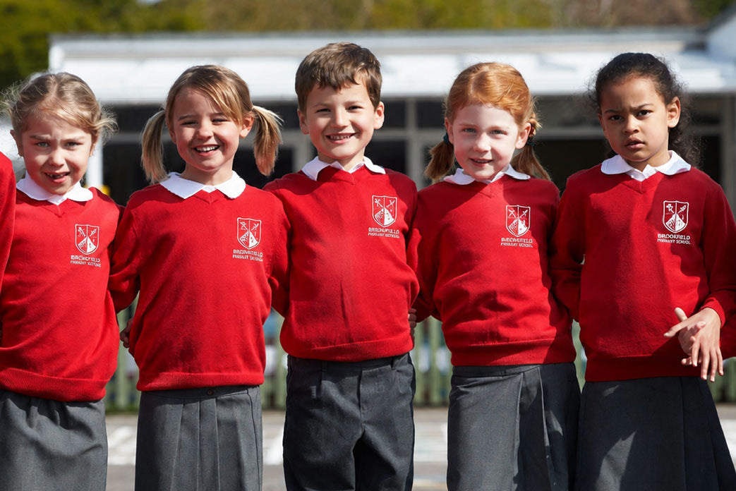 Group of children wearing red sweaters and gray skirts standing in a line.